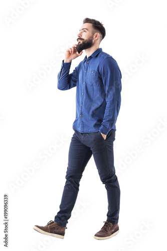 Successful confident business man talking on the phone walking and looking up with hand in pocket. Full body isolated on white background. 