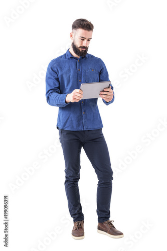 Serious bearded business man holding and watching tablet in both hands. Full body isolated on white background. 