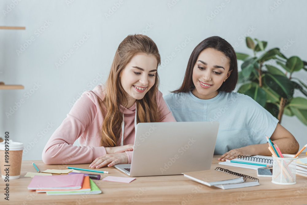 attractive multiethnic students using laptop at table with books attractive multiethnic students using laptop at table with books