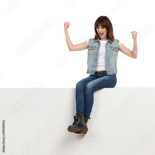 Young Woman Is Sitting On A Top And Shouting With Arms Raised