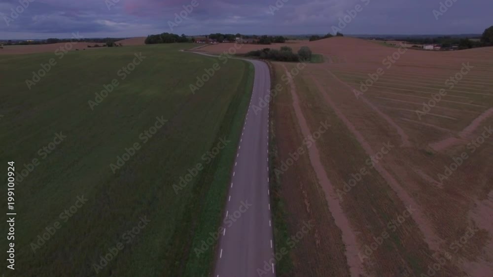 Aerial view of two cars driving on winding road on the countryside. Cinematic drone shot flying over idyllic landscape at dusk in Southern Sweden Aerial view of two cars driving on winding road on the countryside. Cinematic drone shot flying over idyllic landscape at dusk in Southern Sweden