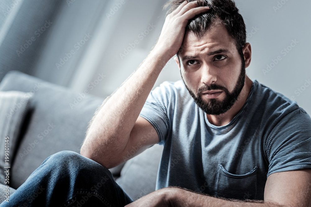 Serious problems. Sad nice young man holding his forehead and thinking about his life while being in a difficult situation Serious problems. Sad nice young man holding his forehead and thinking about his life while being in a difficult situation