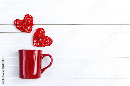 Red coffee mug with hearts coming out of it  on white wooden background.