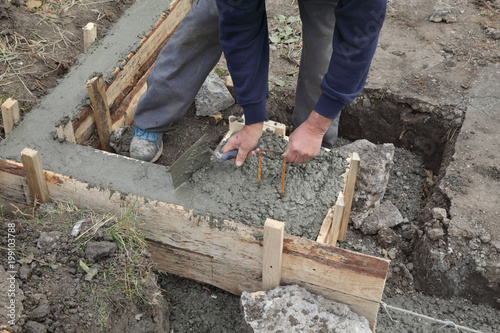 Construction worker making concrete foundation in formwork using trowel photo