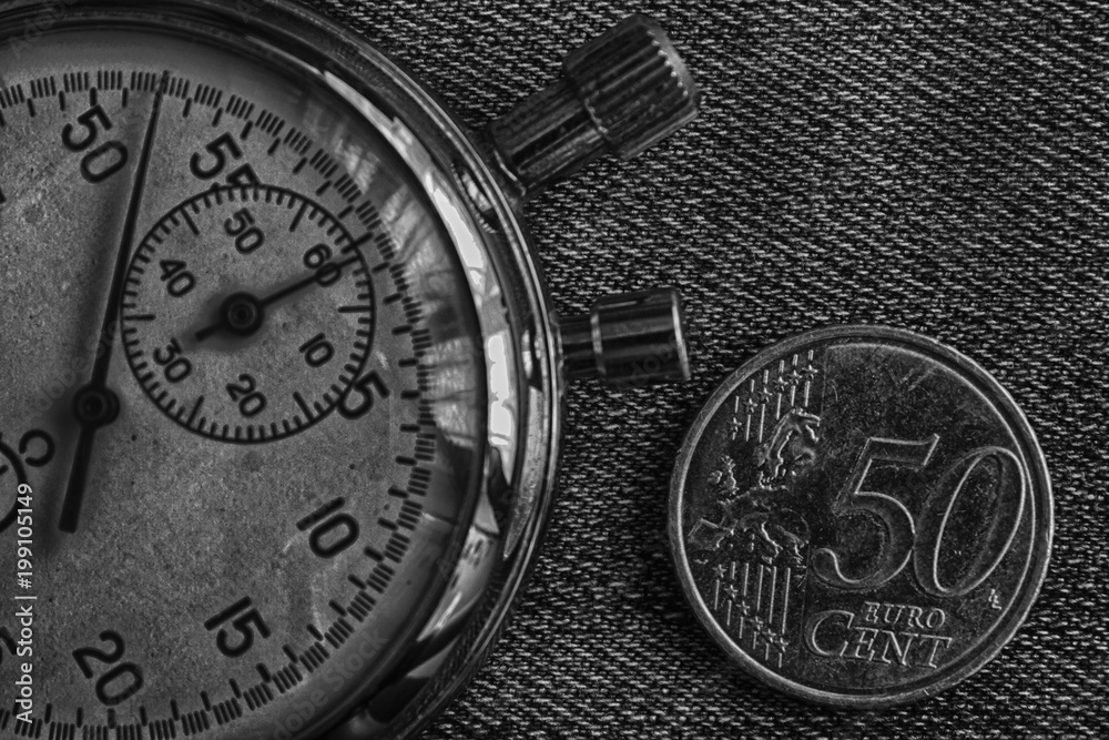 Euro coin with a denomination of 50 euro cents and stopwatch on worn jeans backdrop - business background Euro coin with a denomination of 50 euro cents and stopwatch on worn jeans backdrop - business background