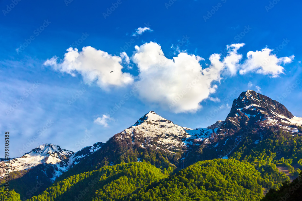Obraz premium Surprisingly beautiful mountain range with melted snow and bright green forest at the foot. The helicopter flies over the valley with a waterfall. Caucasus mountains landscapes, Sochi, Russia.