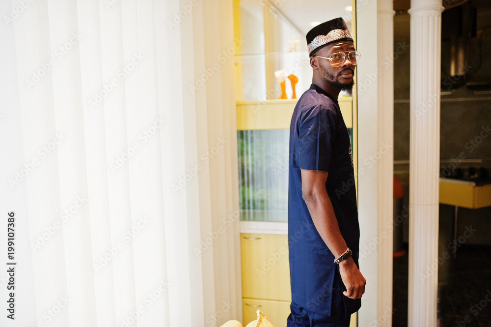 Rich african man in stylish traditional clothes and hat in glasses posed at room . Rich african man in stylish traditional clothes and hat in glasses posed at room .