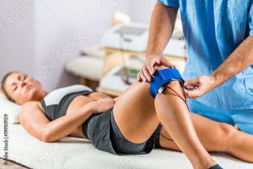 Electrical stimulation in physical therapy. Therapist positioning electrodes onto a patient's knee