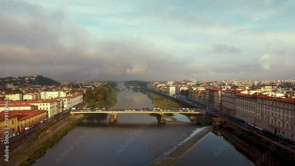 Drone aerial flying down towards a traffic-filled bridge crossing the Arno River in Florence in the evening