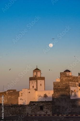 Full moon rising during sunset mosque in Essaouira, Morocco