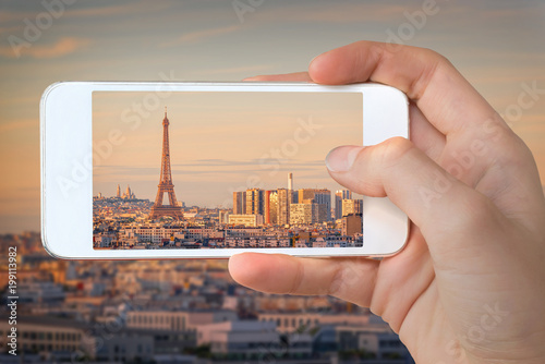 Closeup of a hand with smartphone taking a picture of  Paris with the Eiffel tower at sunset,  France