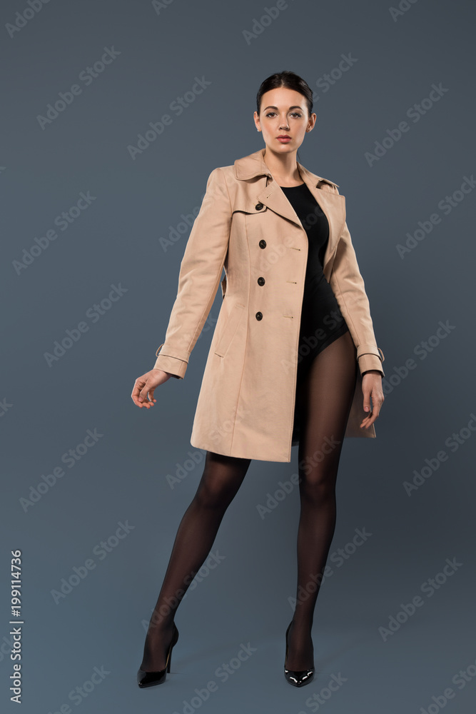 Woman in black pantyhose and heel shoes wearing trench on dark background Woman in black pantyhose and heel shoes wearing trench on dark background