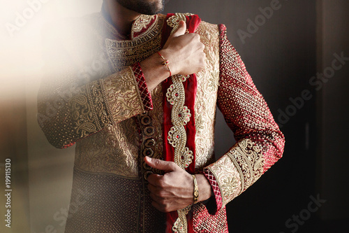 Strong handsome Indian groom holds his hands over wedding suit photo