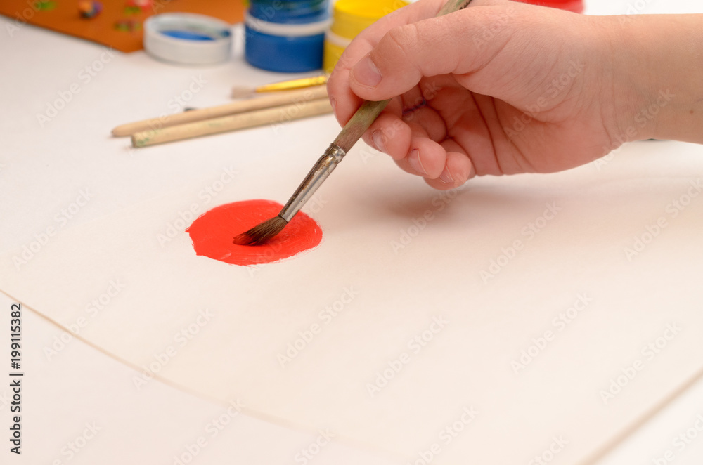 A child's hand draws gouache on white paper with a brush. A child's hand draws gouache on white paper with a brush.