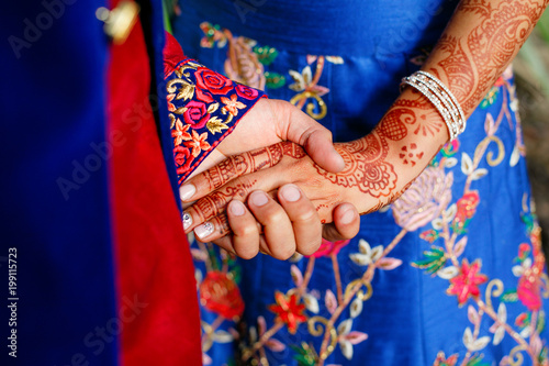 Indian groom holds bride's arm with henna tattoo tender