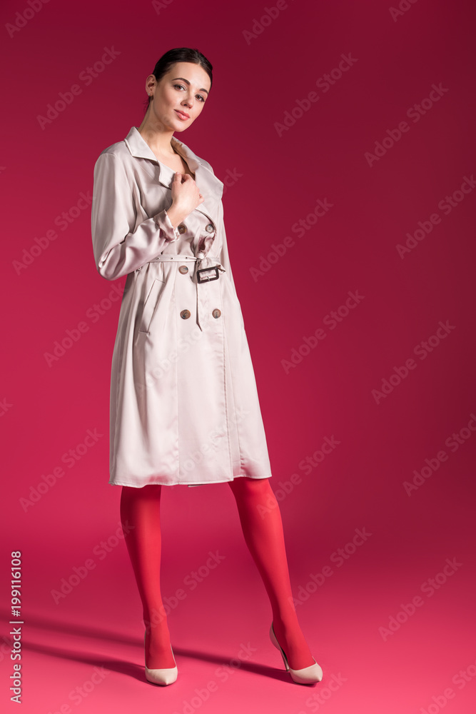 Smiling girl wearing beige trench and high heels on red background Smiling girl wearing beige trench and high heels on red background