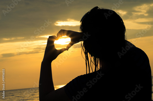 silhouette of a woman with her hands forming a heart, at sunset on the beach