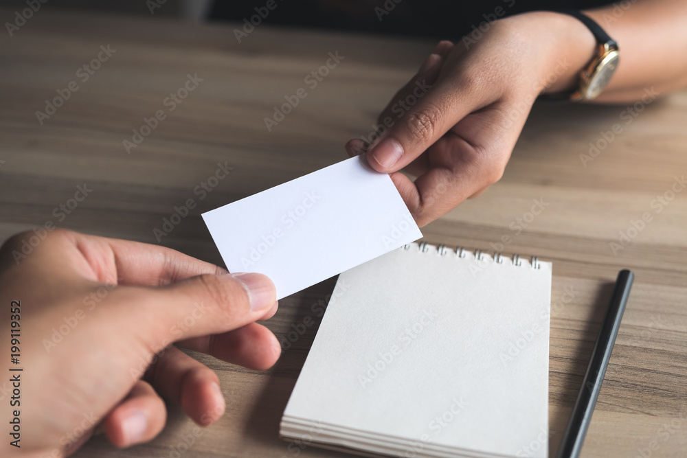 Businessman giving an empty business card to businesswoman with a notebook on wooden table