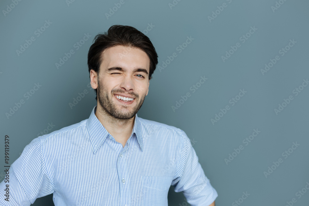 Non verbal language. Cheerful positive happy man smiling and winking while looking at you Non verbal language. Cheerful positive happy man smiling and winking while looking at you