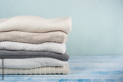 Knitted wool sweaters. Pile of winter clothes on green wooden background, , knitwear, space for text.
