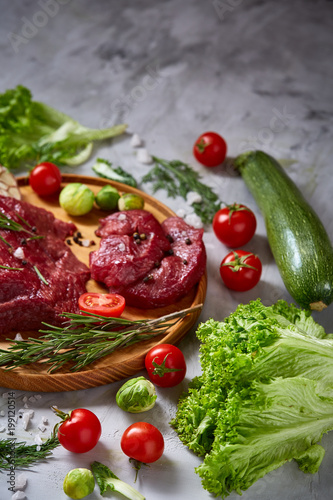 Still life of raw beef meat with vegetables on wooden plate over white background, top view, selective focus