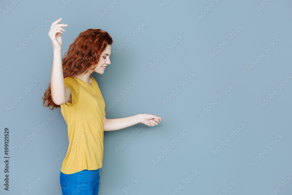 Graphic design. Nice delighted pleasant woman smiling and looking at some object while standing against grey background Graphic design. Nice delighted pleasant woman smiling and looking at some object while standing against grey background