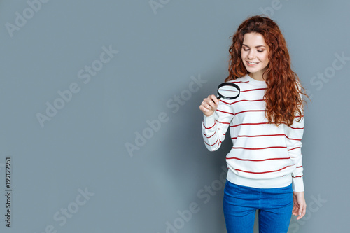 Biological research. Positive smart nice woman smiling and holding a magnifying glass while looking into it