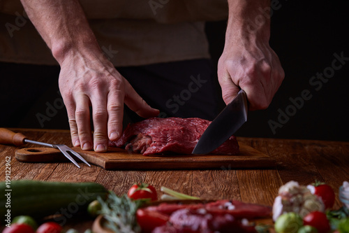 Strong professional man's hands cutting raw beefsteak, selective focus, close-up