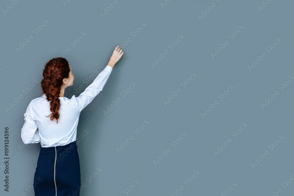 Female teacher. Pleasant smart young woman standing and looking at the wall while writing at it Female teacher. Pleasant smart young woman standing and looking at the wall while writing at it