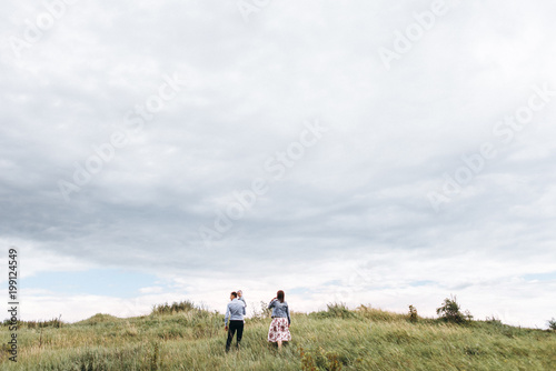 Lifestyle walk of a young family with a little daughter in the mountains along the green grass. Happy family together at outdoors against the sky with clouds. Hands in the hands. Selective focus