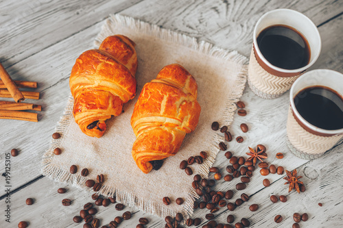 two glasses of black coffee with croissants on a linseed napkin sprinkled with cinnamon and anise on a light wooden table