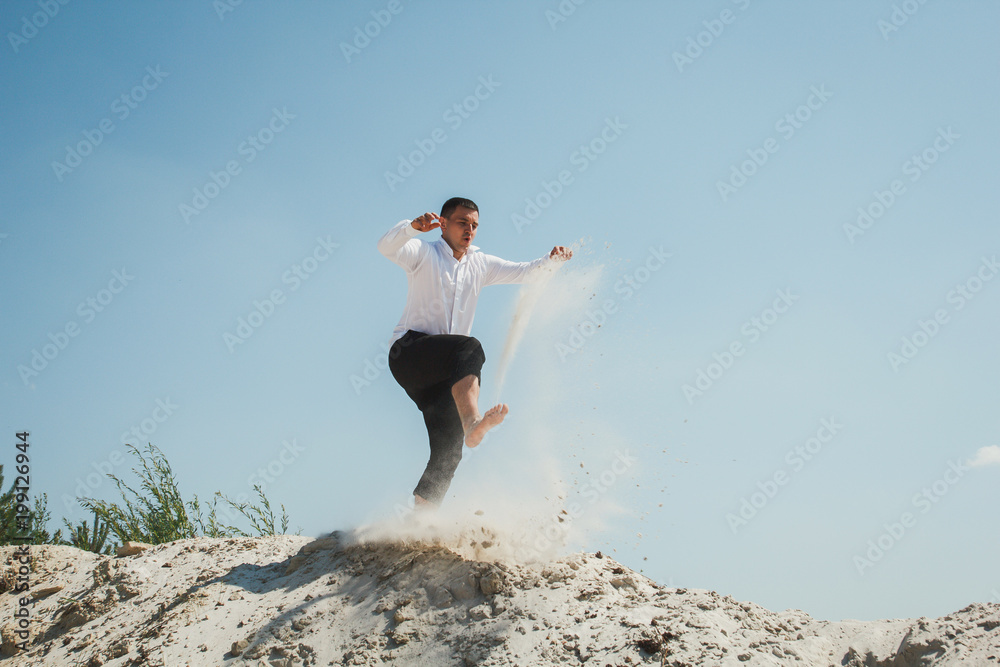 Young man is jumping and running from the white sandy hill. Wedding funny emotional guy photo. Groom is having fun and laugh on the beach. Summer hot weather photo shoot. Young man is jumping and running from the white sandy hill. Wedding funny emotional guy photo. Groom is having fun and laugh on the beach. Summer hot weather photo shoot.