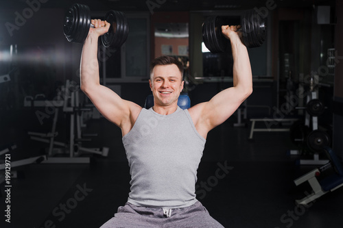 Strong handsome fit man exercising in the gym. Personal trainer workout. Athletic man working out his chest with dumbbells on a bench press. Fitness, healhty lifestyle, bodybuilding concept.