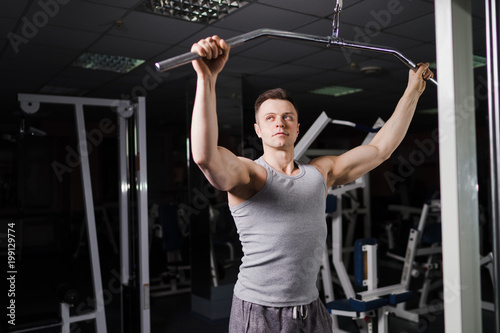 Strong handsome fit man exercising in the gym. Personal trainer workout. Athletic man working out his arms and chest muscles at upper block. Fitness, healhty lifestyle, bodybuilding concept.