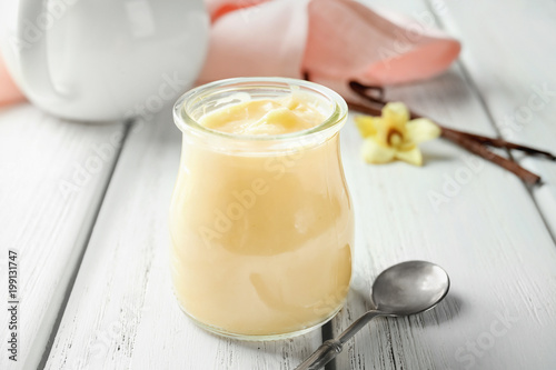 Tasty vanilla pudding in jar on wooden table