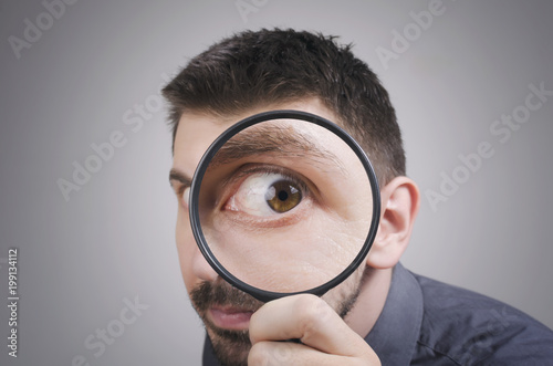 Portrait of a curious man looking through magnifying glass photo