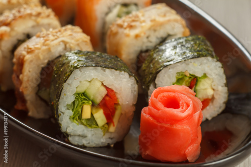 Close up pickled ginger in the form of red rose and sushi rolls - Hosomaki with vegetables, Uramaki with Conger on the background. Japanese cuisine