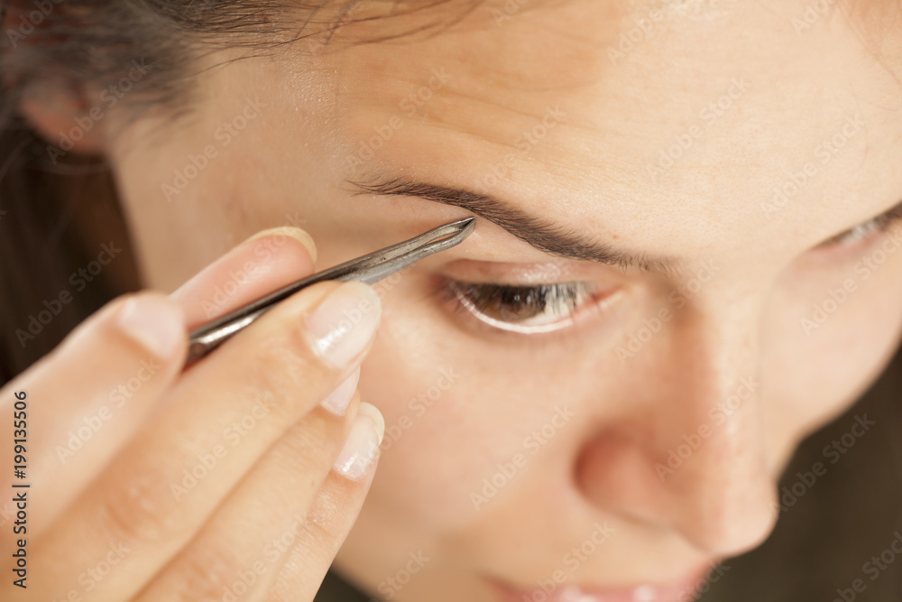 Young beautiful woman pluck her eyebrows with tweezers