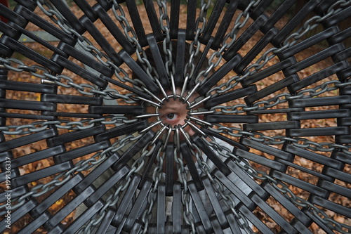 An eye of a young person staring at the viewer through a symmetrical geometric pattern of the bottom of children swings circle