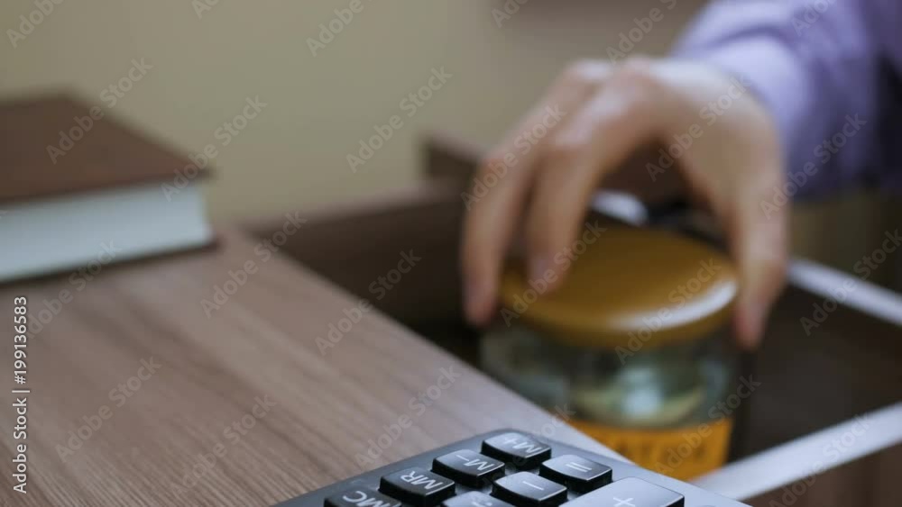 Caucasian male putting a glass jar put in a drawer table with his savings for future vacation Caucasian male putting a glass jar put in a drawer table with his savings for future vacation