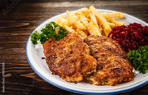 Grilled steak, French fries and vegetables on wooden background