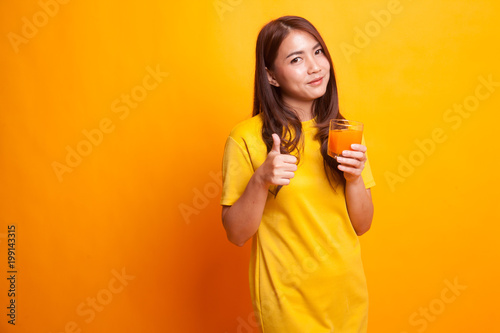 Young Asian woman thumbs up drink orange juice in yellow dress