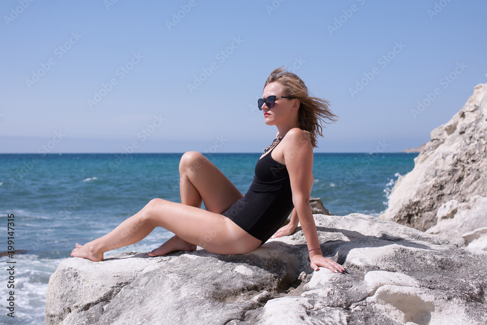 Woman in black bodysuit resting on seashore in windy day