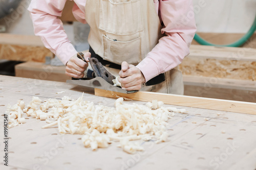 close-up of a male worker in a carpentry shop holds a plane in the hands. on a table of wood are sawdust. joiner's workshop.