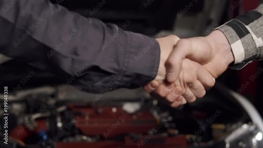 Close Up shot of mechanic and customer shaking hands in an auto repair shop. Close Up shot of mechanic and customer shaking hands in an auto repair shop.