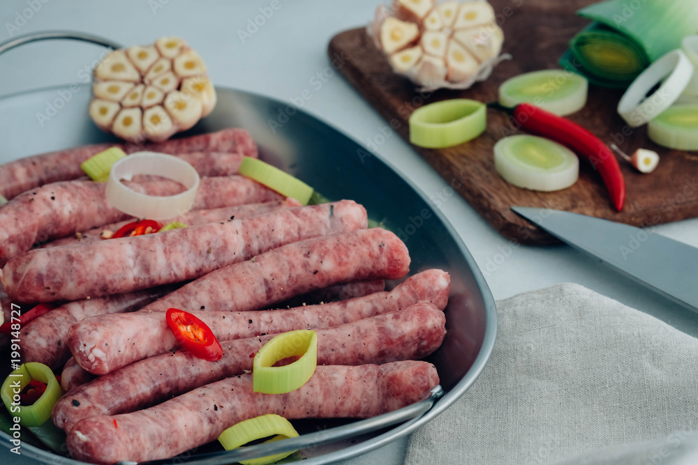 Raw gourmet sausages with fresh herbs, leek and chilli pepper spices on white table. Raw gourmet sausages with fresh herbs, leek and chilli pepper spices on white table.