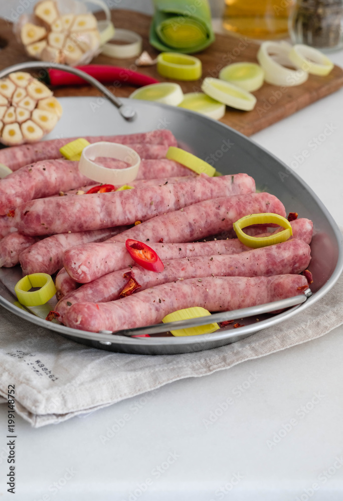 Raw gourmet sausages with fresh herbs, leek and chilli pepper spices on white table.