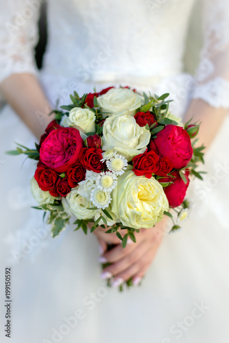 The bride holds a bouquet of red and white roses