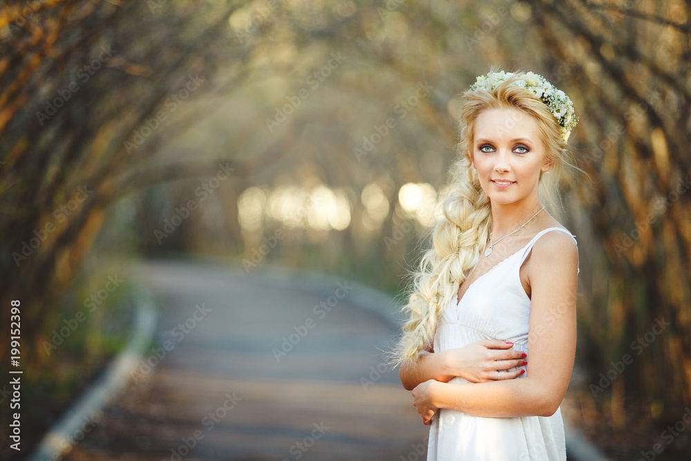 beautiful blond woman in white dress and floral wreath on her head. cute person in alley.