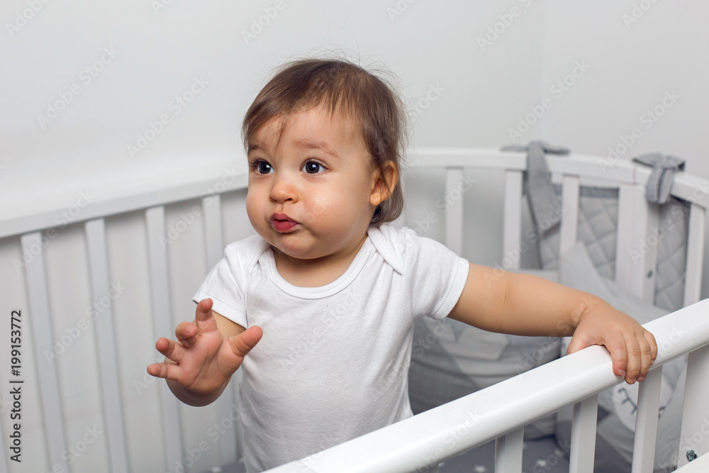 one year old child in white clothes standing in a white round bed in his nursery one year old child in white clothes standing in a white round bed in his nursery